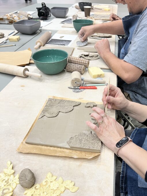 zdjęcie z warsztatów ceramicznych na pierwszym planie prostokątna praca z wypukłymi elementami w tle inne osoby przygotowujace swoje prace